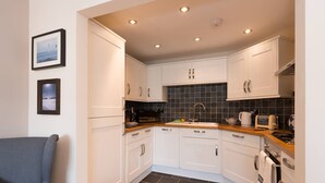 A compact kitchen with white cabinets, a black tiled backsplash, and a wooden countertop. - Bryns Eglwys: Pet-friendly two bed holiday apartment in Rhosneigr (Rhosneigr)