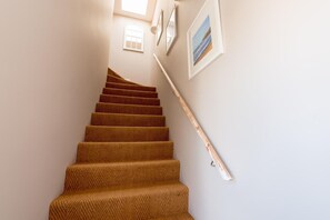 Un escalier recouvert d’une moquette à motifs en chevrons, avec une main courante et des tableaux encadrés accrochés au mur.