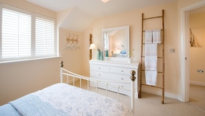 A bedroom with a bed, dresser, mirror, and a ladder for hanging clothes. - Bryns Eglwys: Pet-friendly two bed holiday apartment in Rhosneigr (Rhosneigr)