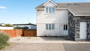 A two-story house with a white exterior, a stone facade on the right, and a paved driveway. - Bryns Eglwys: Pet-friendly two bed holiday apartment in Rhosneigr (Rhosneigr)
