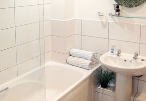 A bathroom with a bathtub, a sink, and a glass shelf with toiletries.