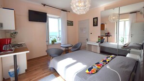 Une chambre avec un lit, un bureau, une chaise, une télévision et un balcon avec vue.