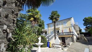 Un bâtiment doté d’un escalier en pierre menant à un balcon, entouré de palmiers et agrémenté d’une fontaine.