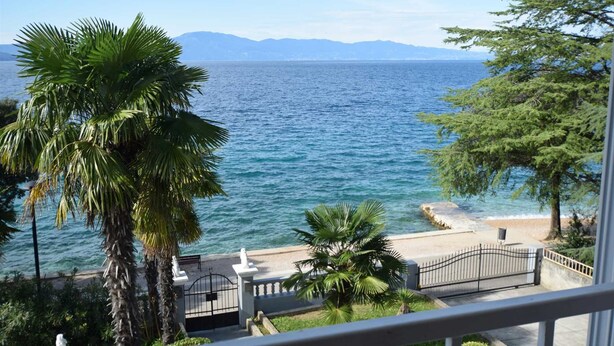Un balcon offrant une vue sur la mer, des palmiers et un chemin de pierre menant à une porte.