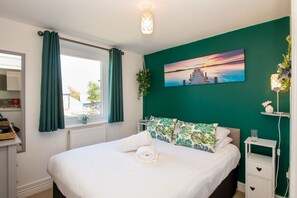 A bedroom with a bed, a window with curtains, a wall-mounted painting, and a bedside table with a lamp. - Bwthyn Siwan: Two bedroom, pet-friendly holiday cottage (Ty Croes)
