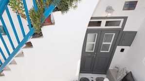 A white building with a blue staircase, a grey door with windows, and a small outdoor seating area with cushions.