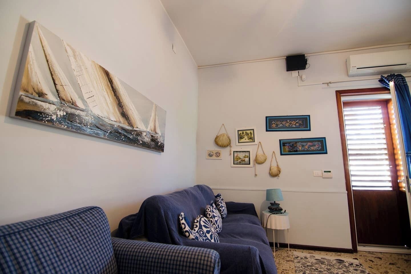 Ein Wohnzimmer mit einer Couch, einem Gemälde, Wanddekorationen und einer Tür mit Jalousien.
