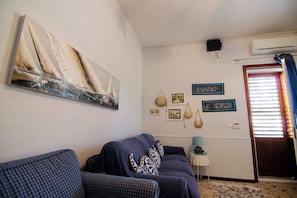 Un salón con sofá, un cuadro, adornos en la pared y una puerta con persianas.