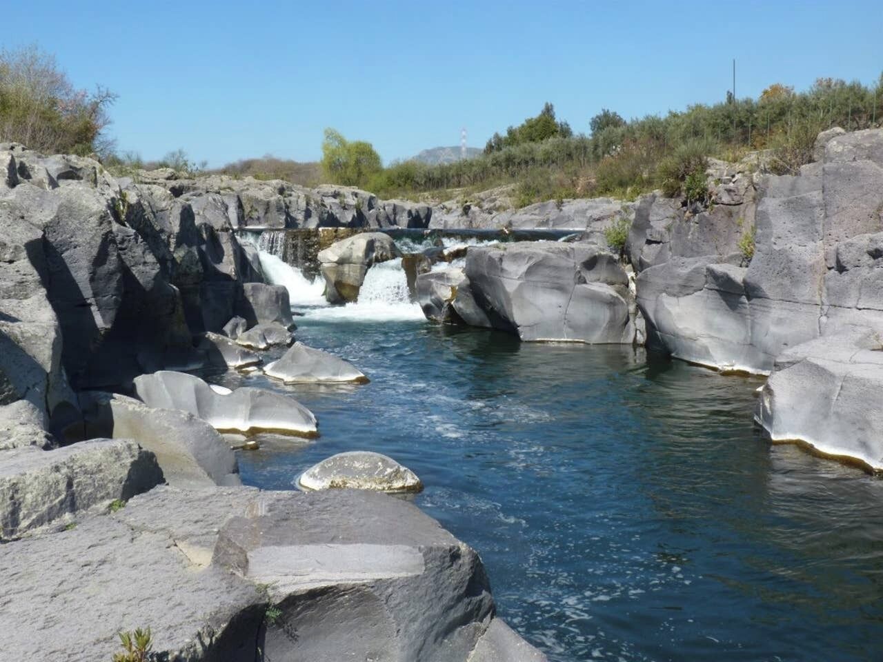 Eine natürliche Landschaft mit einem Wasserfall, felsigem Gelände und einem Fluss.