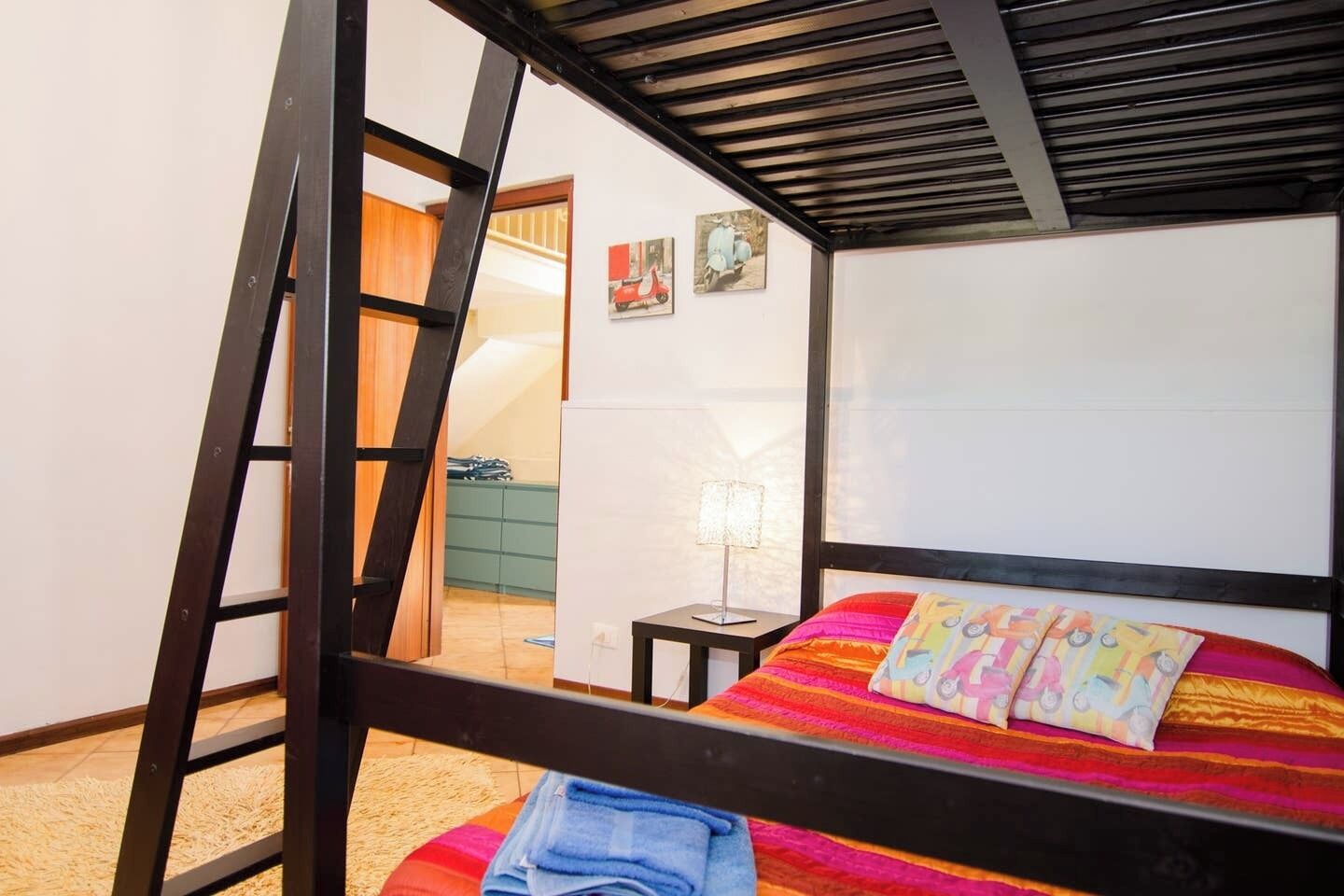 Una cama individual superpuesta con una escalera, una mesita de noche con una lámpara y una pared decorada con dos cuadros.