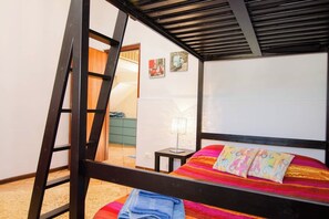 Uma cama beliche com escada, uma mesa de cabeceira com abajur e uma parede com duas imagens emolduradas.