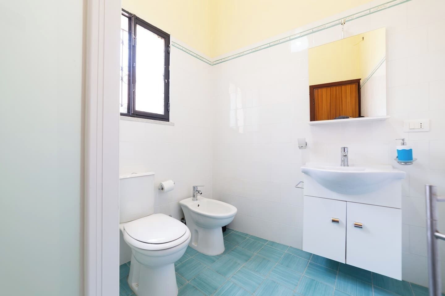 Un baño con inodoro, bidé y lavamanos con espejo superior.
