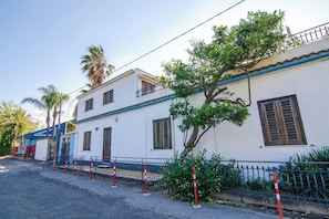 Ein zweistöckiges Gebäude mit weißer Fassade, mehreren Fenstern mit Fensterläden und einem Balkon.
