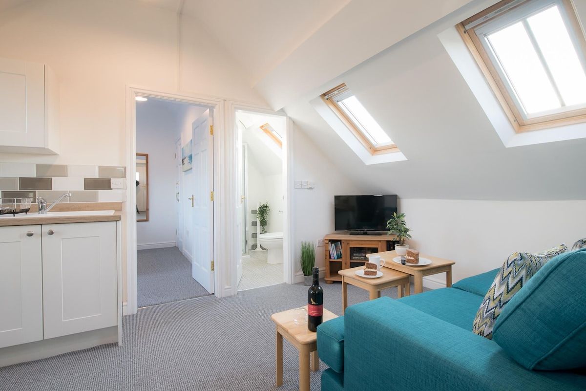 A compact living space with a kitchenette, a sofa, a television, and skylights.
