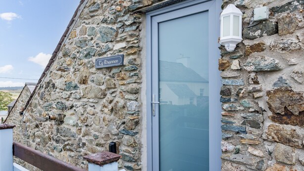 Ein Steinhaus mit einem Schild, auf dem "Rhaannon" steht, und einer Glastür.