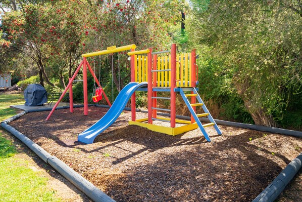 Un parque infantil con tobogán, estructura de escalada y columpios.