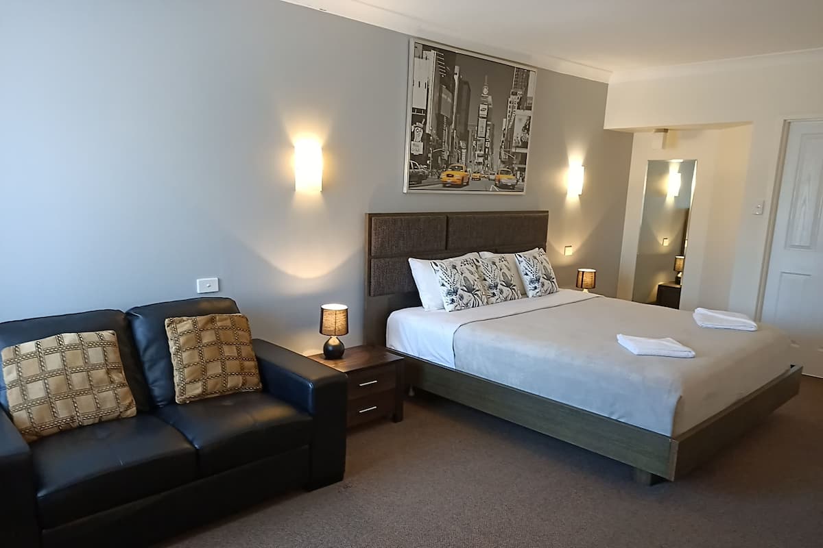 Ein Hotelzimmer mit einem Bett, einer Couch, einem Nachttisch mit Lampe und einem Bild an der Wand.