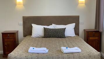 A neatly made bed with a patterned bedspread, two pillows, and two folded towels.