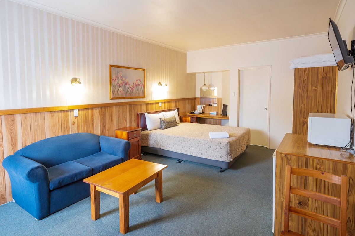 Ein Hotelzimmer mit Bett, blauem Sofa, Holztisch, Schreibtisch und Fernseher.