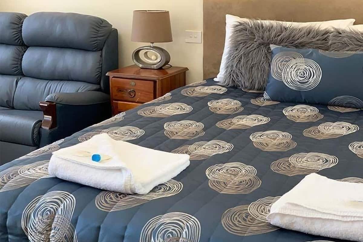 Ein Hotelzimmer mit Bett, Sessel, Nachttisch und Lampe.