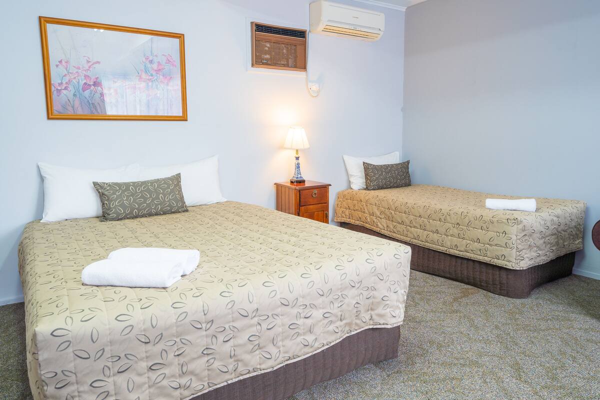Ein Hotelzimmer mit zwei Betten, einem Nachttisch mit Lampe, einer Klimaanlage und einem gerahmten Bild an der Wand.