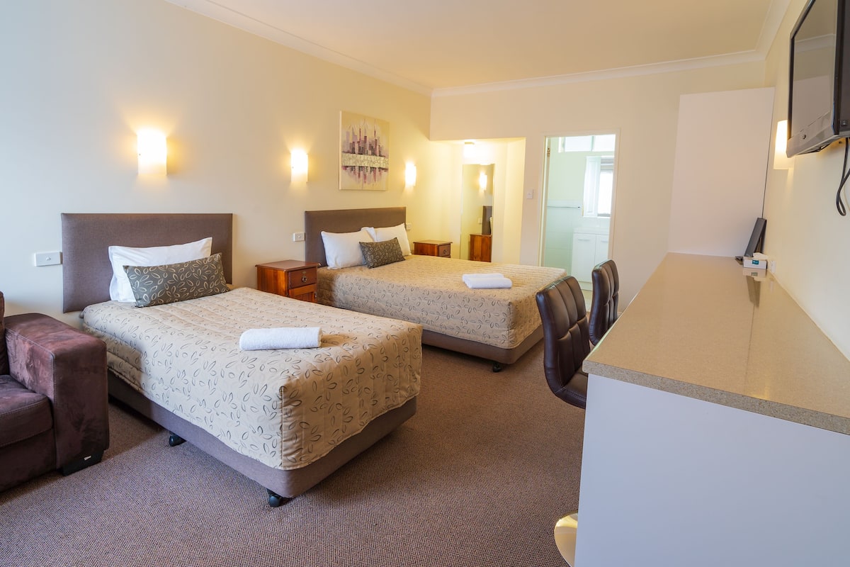 Ein Hotelzimmer mit zwei Betten, einem Sofa, einem Schreibtisch und einem Fernseher.