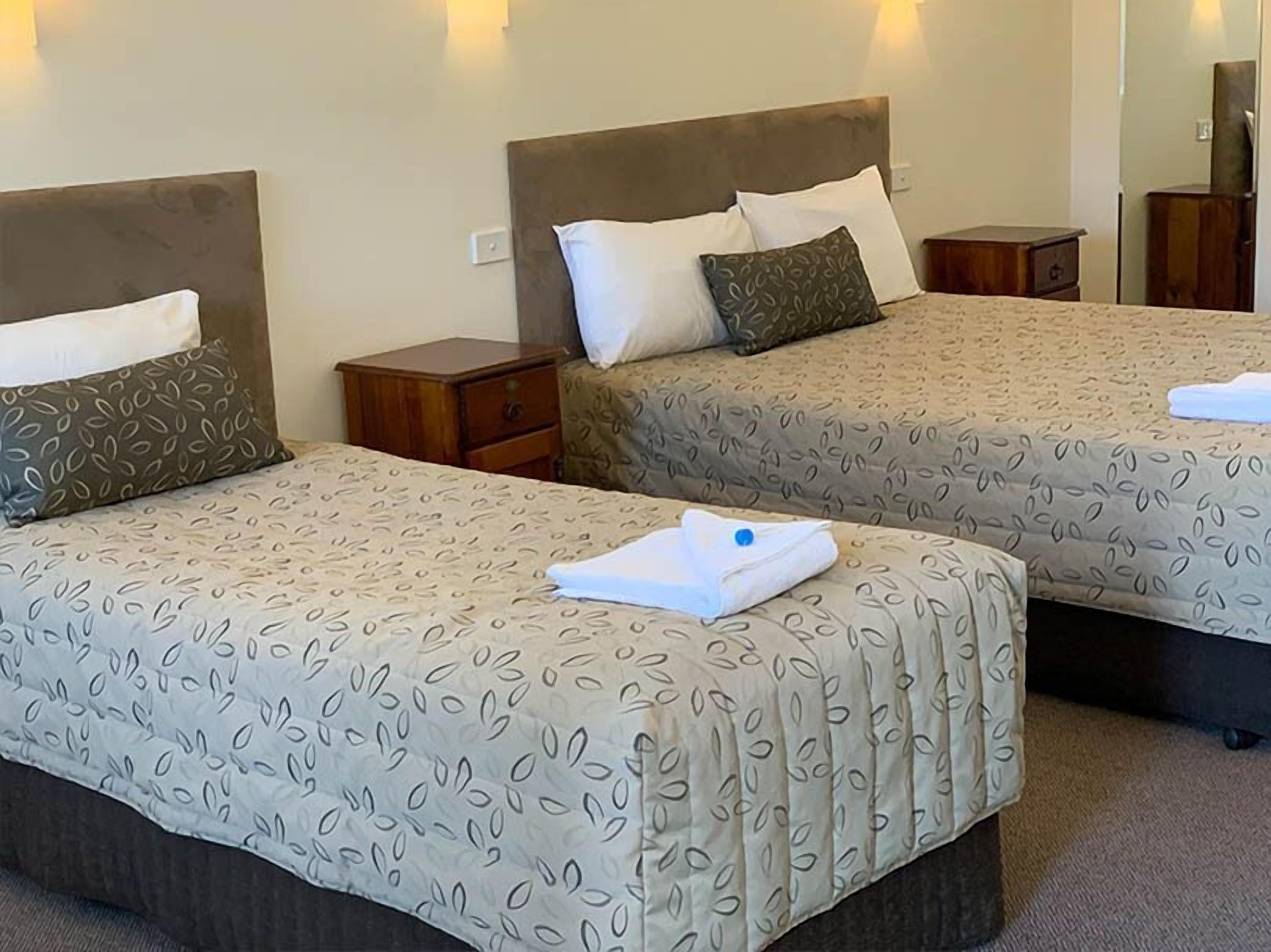 Two double beds with matching headboards and footboards, a small wooden nightstand, and a wall-mounted light fixture.