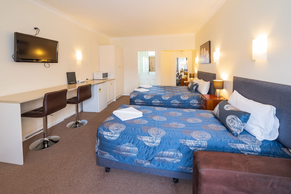 Ein Hotelzimmer mit zwei Betten, einem Schreibtisch mit Stühlen, einem Fernseher und einem durchgegangene Tür erkennbaren Badezimmer.
