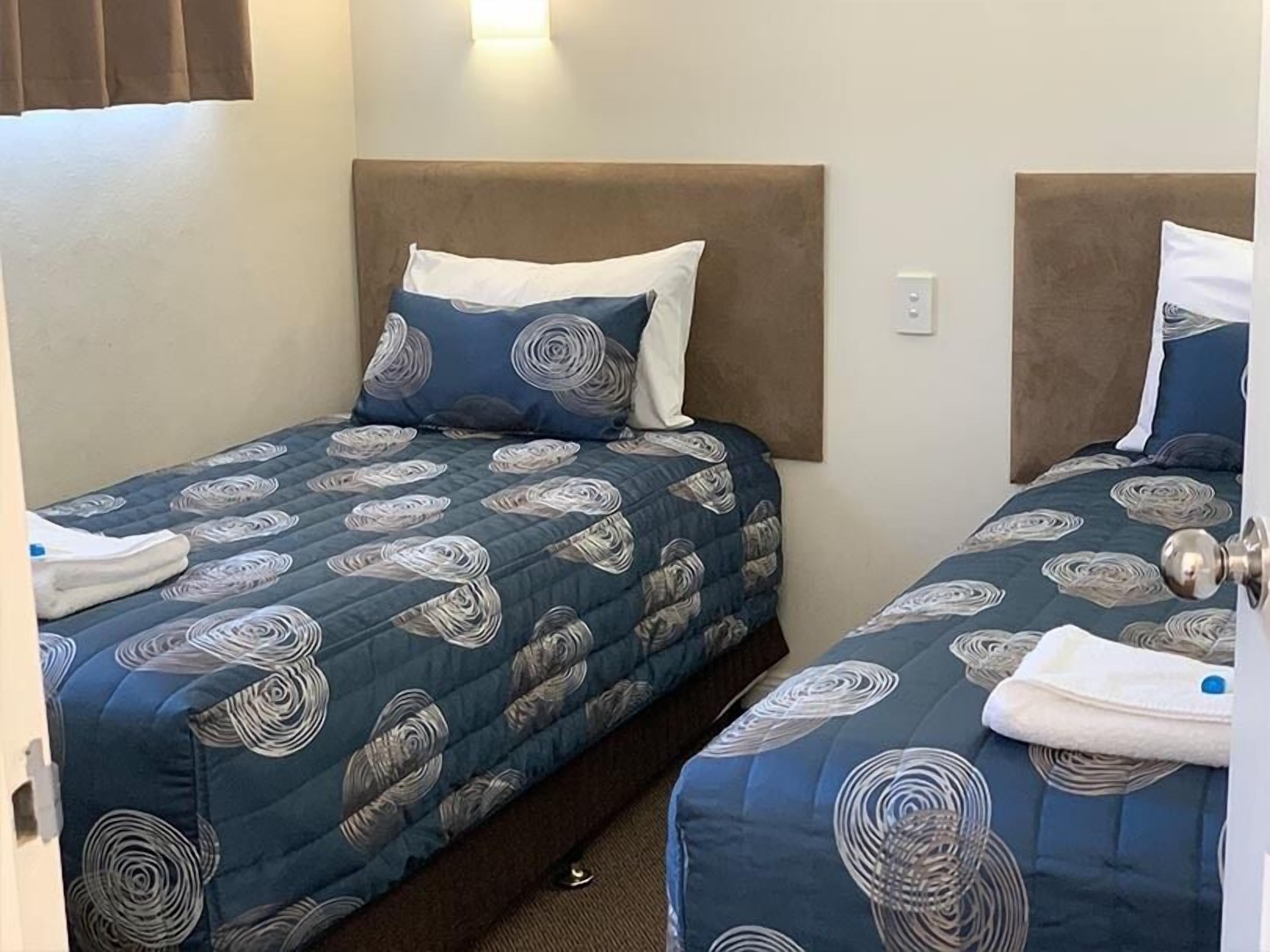 Ein Hotelzimmer mit zwei Einzelbetten, jeweils mit einem Kopfteil, einer Daunendecke mit Wirbelmuster und einem weißen Kopfkissen.