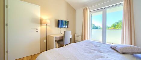 A hotel room with a bed, a desk, a chair, a TV, and a large window with curtains.