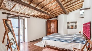 A bedroom with a wooden ceiling, a bed with a striped bedspread, a wooden wardrobe, and a large mirror.