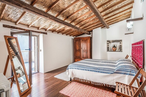 A bedroom with a wooden ceiling, a bed with a striped bedspread, a wooden wardrobe, and a large mirror.