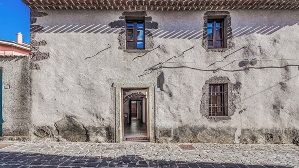 A rustic building with a cobblestone street, a central doorway, and two windows with shutters.