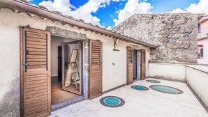 A rooftop with a stone wall, wooden shutters, and a pool area with circular tiles.