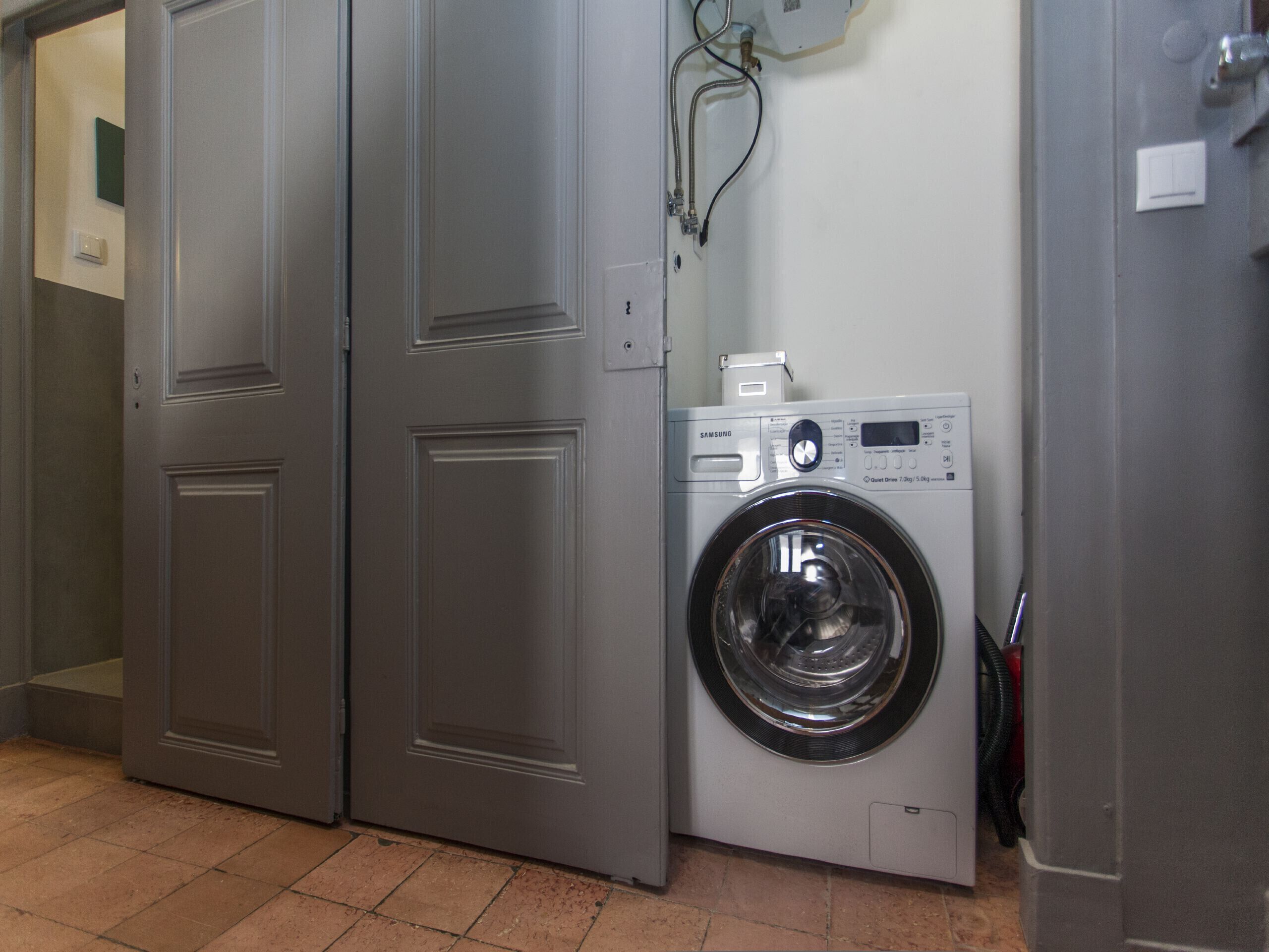 A laundry room with a front-loading washing machine, a door, and a wall-mounted electrical outlet.