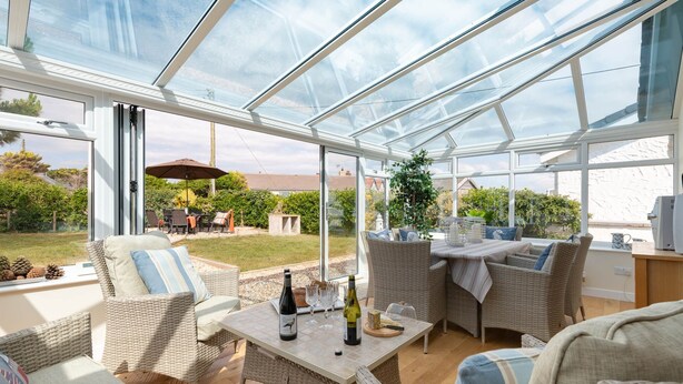 Ein Wintergarten mit Korbmöbeln, einem Tisch mit Weinflaschen und Blick auf den Garten.