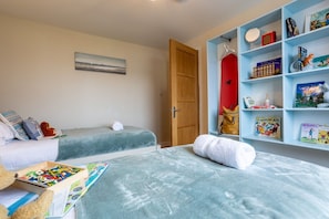 Une chambre avec deux lits, une bibliothèque remplie de livres pour enfants et une porte.