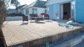 Eine Holzterrasse mit Gartenmöbeln, einem Schild mit der Aufschrift 'PEN Y BRYN' und einem Haus im Hintergrund.