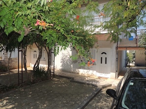 A residential building with a paved driveway, a parked car, and a tree with red flowers. - Apartment Dragica 1  with terrace (Malinska)