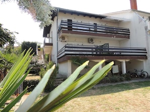 A two-story building with balconies, a bicycle parked outside, and a garden in the foreground. - Apartment Dragica 1  with terrace (Malinska)