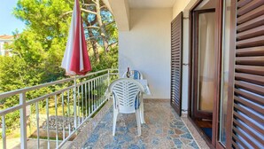 A balcony with a white chair, a small table with a bottle, and a red and white umbrella. - Studio Apartment Vlatko 2 (Krk)