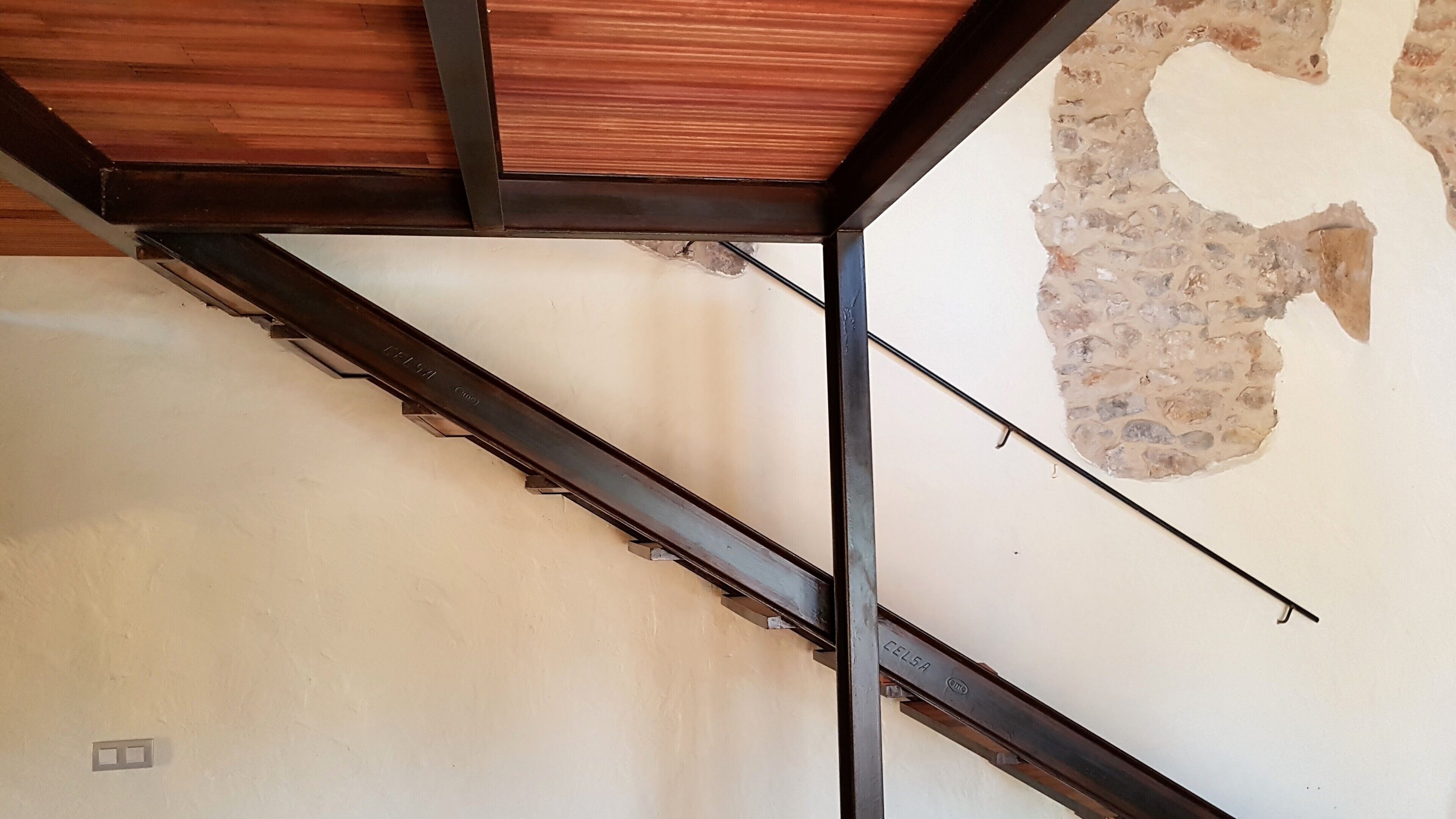 A room with exposed ceiling beams and a damaged wall section.