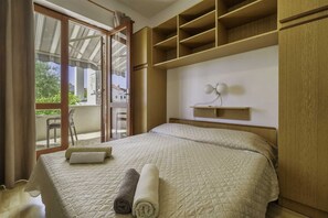 Een slaapkamer met een bed, een raam, een stoel en een wandplank.