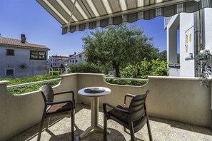 Un balcón con dos sillas y una mesa pequeña, con vistas a una zona residencial con árboles y edificios.