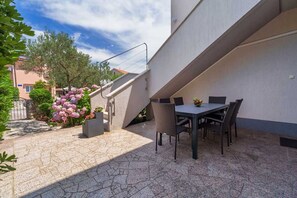 Une terrasse extérieure avec une table et des chaises, un sol en pierre et un escalier menant à un niveau supérieur.