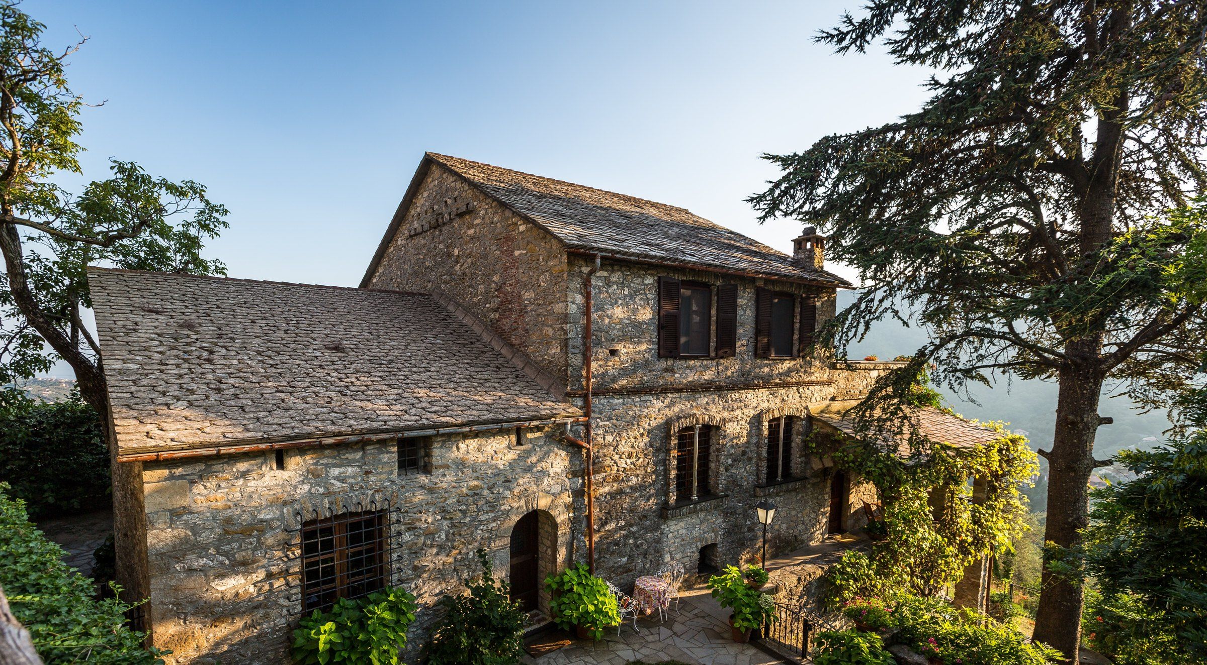 A stone building with a sloped roof, multiple windows, and a small outdoor seating area with a table and chairs.