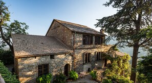 Un bâtiment en pierre avec un toit en pente, de nombreuses fenêtres et un petit espace extérieur aménagé avec une table et des chaises.