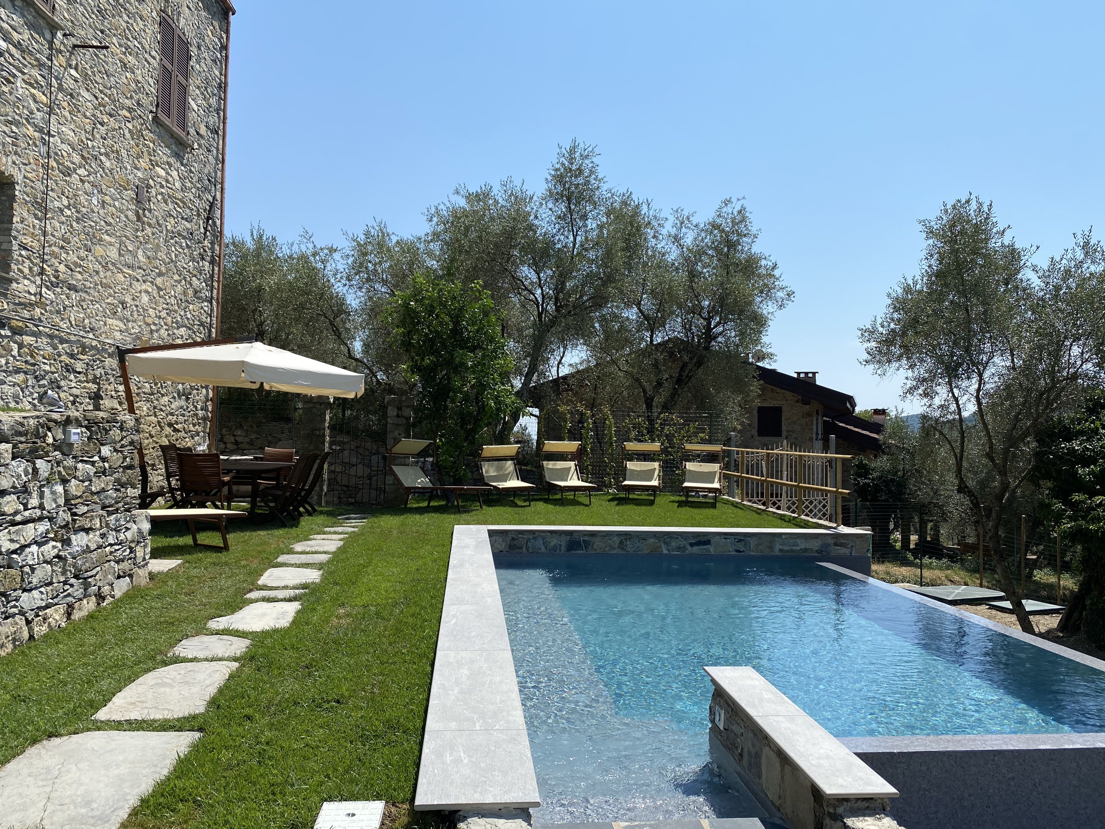 Un edificio de piedra con piscina, mobiliario de exterior y zona ajardinada.