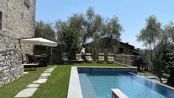 Un edificio de piedra con piscina, mobiliario de exterior y zona ajardinada.