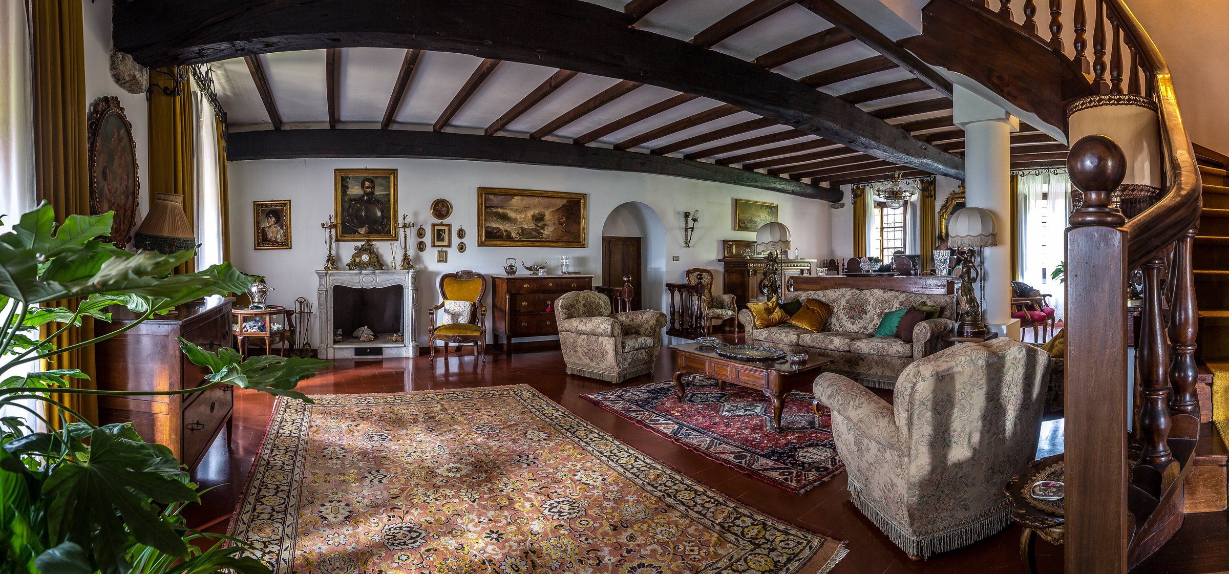 A traditional room with a fireplace, multiple armchairs, a patterned rug, and a staircase with wooden balusters.